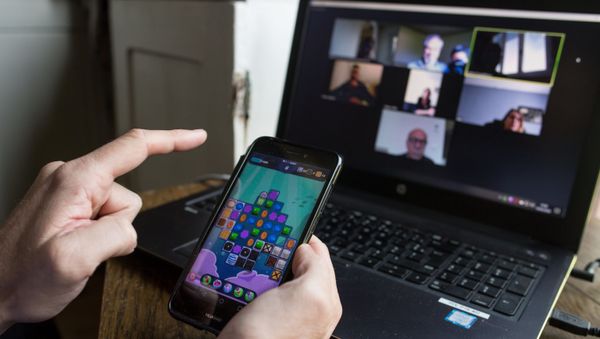 A man plays a game on his smart phone during a video conference as he works from home, on May 14, 2020 in Vertou, outside Nantes, as France eases lockdown measures taken to curb the spread of the COVID-19 pandemic, caused by the novel coronavirus. - Sputnik International