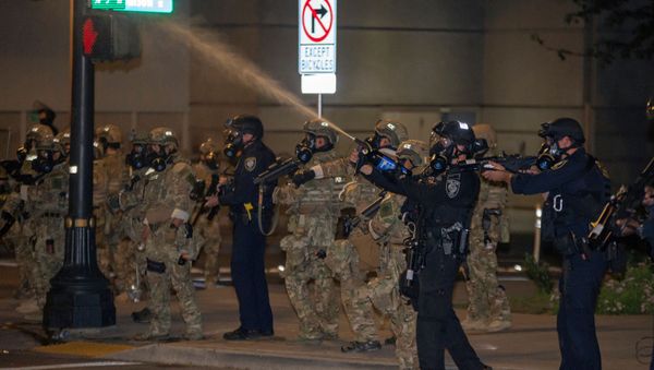 A federal law enforcement officer, deployed under the Trump administration's new executive order to protect federal monuments and buildings, shoots pepper spray into the air during a protest against racial inequality in Portland, Oregon, U.S. July 17, 2020. Picture taken July 17, 2020 - Sputnik International
