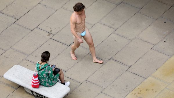 A man wearing a surgical mask as G-string walks past a woman, as the spread of the coronavirus disease (COVID-19) continues, on Oxford Street in London, Britain July 24, 2020 - Sputnik International