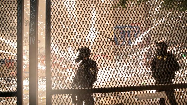 Federal law enforcement officers stand behind a metal fence as demonstrators are approaching during a protest against racial inequality and police violence in Portland, Oregon, U.S., July 25, 2020. - Sputnik International
