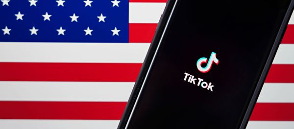 In this photo illustration, a mobile phone featuring the TikTok app is displayed next to the American flag on August 03, 2020 in New York City. Under threat of a U.S. ban on the popular social media app, it has been reported that Microsoft is considering taking over from Chinese firm ByteDance. - Sputnik International