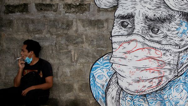 A man smokes a cigarette next to a mural of a man wearing a protective mask amid the coronavirus disease (COVID-19) outbreak in Quezon City, Metro Manila, Philippines, July 30, 2020. A man smokes a cigarette next to a mural of a man wearing a protective mask amid the coronavirus disease (COVID-19) outbreak in Quezon City, Metro Manila, Philippines, July 30, 2020. - Sputnik International