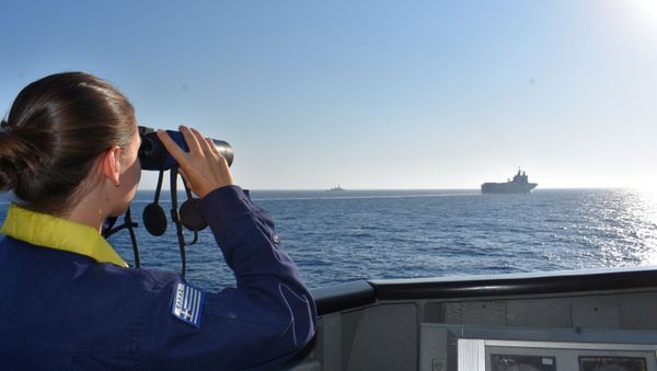 A woman looks through binoculars as Greek and French vessels sail in formation during a joint military exercise in Mediterranean sea, in this undated handout image obtained by Reuters on August 13, 2020 - Sputnik International