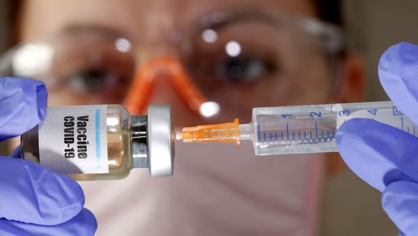 A woman holds a small bottle labeled with a Vaccine COVID-19 sticker and a medical syringe in this illustration taken April 10, 2020. - Sputnik International