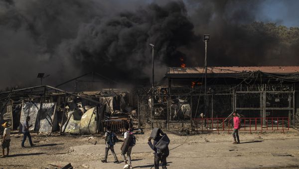 People walk past a fire raging in the camp of Moria on the island of Lesbos after a major fire broke out, on September 9, 2020. - Sputnik International