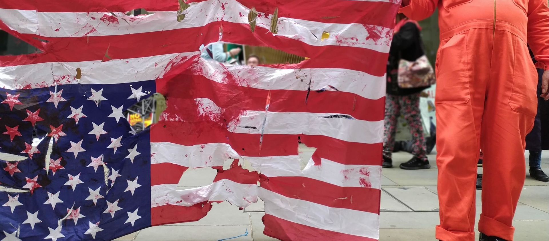 Tattered US flag upside-down with protester in orange jumpsuit holding placard with Hands Off Assange message - Sputnik International, 1920, 09.09.2020