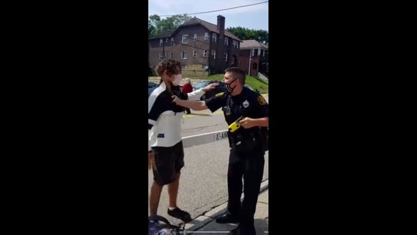 Screenshot captures moment in which an officer with Pennsylvania's Pittsburgh Bureau of Police placed a local resident under arrest for questioning his choice of face mask. At the time the officer was sporting a mask that was designed with the American flag; however, it was embroidered with a blue line - an image used as part of a pro-police movement in response to the Black Lives Matter movement. - Sputnik International