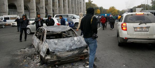 People are seen next to a car burnt during a protest against the results of a parliamentary election in Bishkek, Kyrgyzstan, October 6, 2020 - Sputnik International