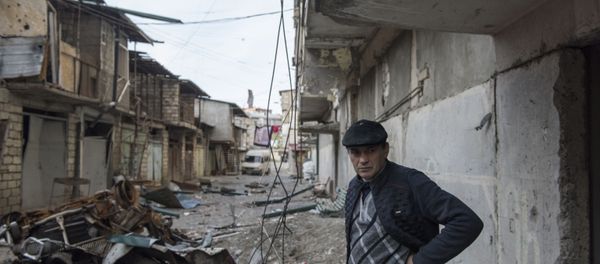 A man stands near a house with a row of destroyed barns in the background in Stepanakert, a self-proclaimed Republic of the Nagorno-Karabakh.  - Sputnik International