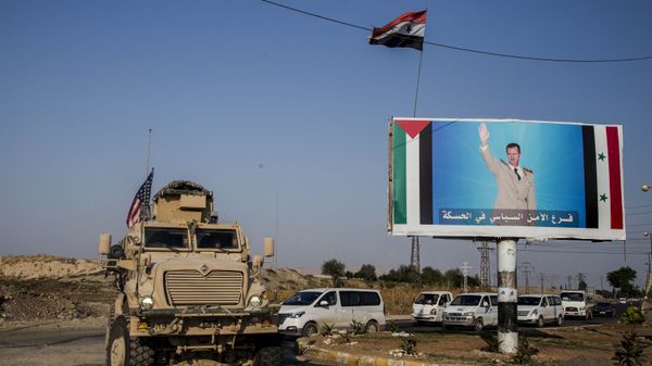 FILE - In this Saturday, 26 October 2019 file photo, a US military vehicle drives south of the northeastern city of Qamishli, likely heading to the oil-rich Deir el-Zour area where there are oil fields, or possibly to another base nearby, as it passes by a poster showing Syrian President Bashar Assad. FILE - In this Saturday, 26 October 2019 file photo, a US military vehicle drives south of the northeastern city of Qamishli, likely heading to the oil-rich Deir el-Zour area where there are oil fields, or possibly to another base nearby, as it passes by a poster showing Syrian President Bashar Assad. - Sputnik International
