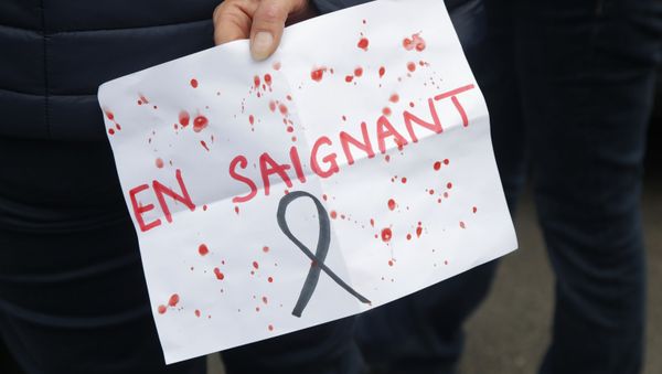 A person holds a poster reading Bleeding, playing with the French word for Teacher, outside the school where a slain history teacher was working, 17 October 2020 in Conflans-Sainte-Honorine, northwest of Paris - Sputnik International