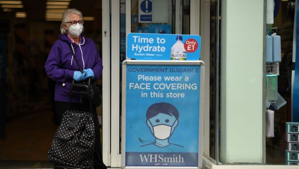 A shopper wearing a face mask stands alongside a sign calling for the wearing of face coverings in shops, in the city centre of Sheffield, south Yorkshire on July 24, 2020, as lockdown restrictions continue to be eased during the novel coronavirus COVID-19 pandemic - Sputnik International
