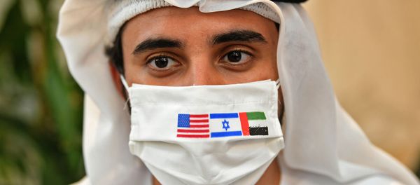 A picture taken on August 31, 2020, shows an Emirati man, wearing a protective mask with the flags of the US, Israel and the UAE, ahead of the arrival of the first commercial flight from Israel, carrying a US-Israeli delegation to the UAE following a normalisation accord, at the Abu Dhabi airport - Sputnik International