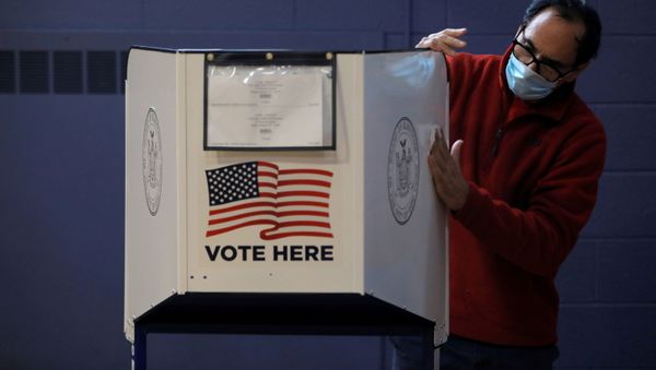 A man sanitizes a privacy booth to fight the spread of coronavirus disease (COVID-19) at a polling station opened for early voting at Our Lady Help of Christians in Staten Island, New York City, US, October 25, 2020 - Sputnik International