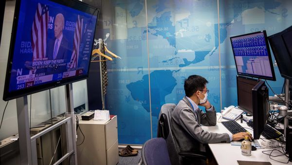 A currency trader works at his desk as a screen (L) shows news updates on the US presidential election featuring an image of Democratic Party candidate Joe Biden, at a foreign exchange trading company in Tokyo on November 5, 2020 - Sputnik International
