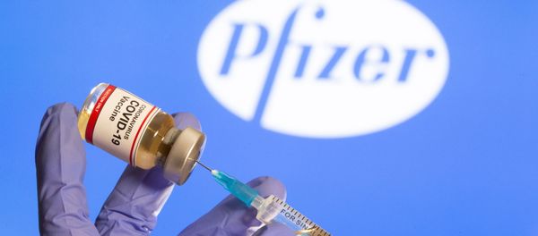 A woman holds a small bottle labelled with a Coronavirus COVID-19 Vaccine sticker and a medical syringe in front of displayed Pfizer logo in this illustration taken, October 30, 2020. - Sputnik International