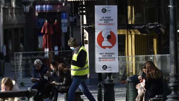 A man wears a face mask as he walks past a sign reading 'wearing a mask is mandatory' on a street in Brussels on November 6, 2020, placed in an attempt to counter the spread of the coronavirus (Covid-19) pandemic. - Sputnik International
