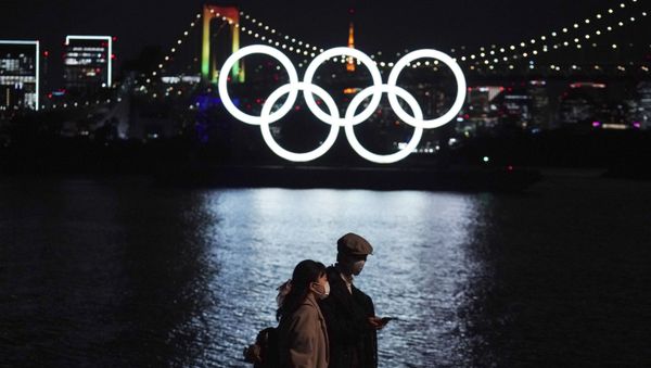 A man and woman walk past the Olympic rings floating in the water in the Odaiba (artificial island) section on Tuesday, 1 December 2020, in Tokyo. The Olympic Symbol was reinstated after it was taken down for maintenance ahead of the postponed Tokyo 2020 Olympics. - Sputnik International