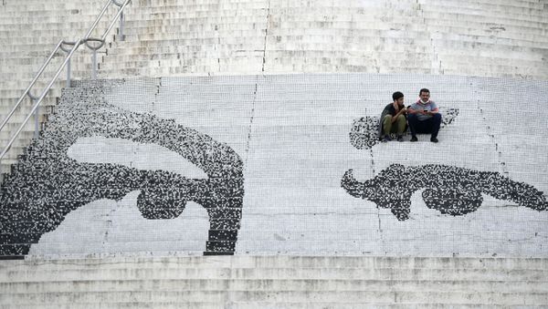 A father and son sit on a set of steps that have the eyes of the late President Hugo Chavez painted on them during elections to choose members of the National Assembly in Caracas, Venezuela, Sunday, Dec. 6, 2020 - Sputnik International