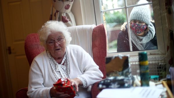Nicky Clough looks through the window at her mother Pam Harrison opening a present on Christmas Day at Alexander House Care Home, as the spread of the coronavirus disease (COVID-19) continues, in Wimbledon, London, Britain, December 25, 2020 - Sputnik International