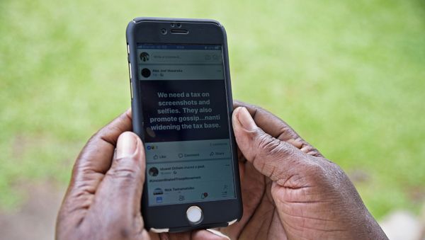 A woman reads a message on social media tax as she scrolls through her Facebook account on her phone in Kampala on July 5, 2018 - Sputnik International