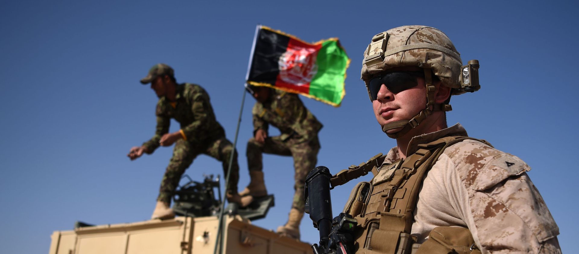 In this photograph taken on August 28, 2017, a US Marine looks on as Afghan National Army soldiers raise the Afghan National flag on an armed vehicle during a training exercise to deal with IEDs (improvised explosive devices) at the Shorab Military Camp in Lashkar Gah in Helmand province. - Marines in Afghanistan's Helmand say Donald Trump's decision to keep boots on the ground indefinitely gives them all the time in the world to retake the province, once the symbol of US intervention but now a Taliban stronghold. They may need it. At the hot, dusty Camp Shorab, where many of the recently deployed Marines train their Afghan counterparts in flat, desert terrain, the Afghans admit th In this photograph taken on August 28, 2017, a US Marine looks on as Afghan National Army soldiers raise the Afghan National flag on an armed vehicle during a training exercise to deal with IEDs (improvised explosive devices) at the Shorab Military Camp in Lashkar Gah in Helmand province. - Marines in Afghanistan's Helmand say Donald Trump's decision to keep boots on the ground indefinitely gives them all the time in the world to retake the province, once the symbol of US intervention but now a Taliban stronghold. They may need it. At the hot, dusty Camp Shorab, where many of the recently deployed Marines train their Afghan counterparts in flat, desert terrain, the Afghans admit th - Sputnik International, 1920, 16.01.2021