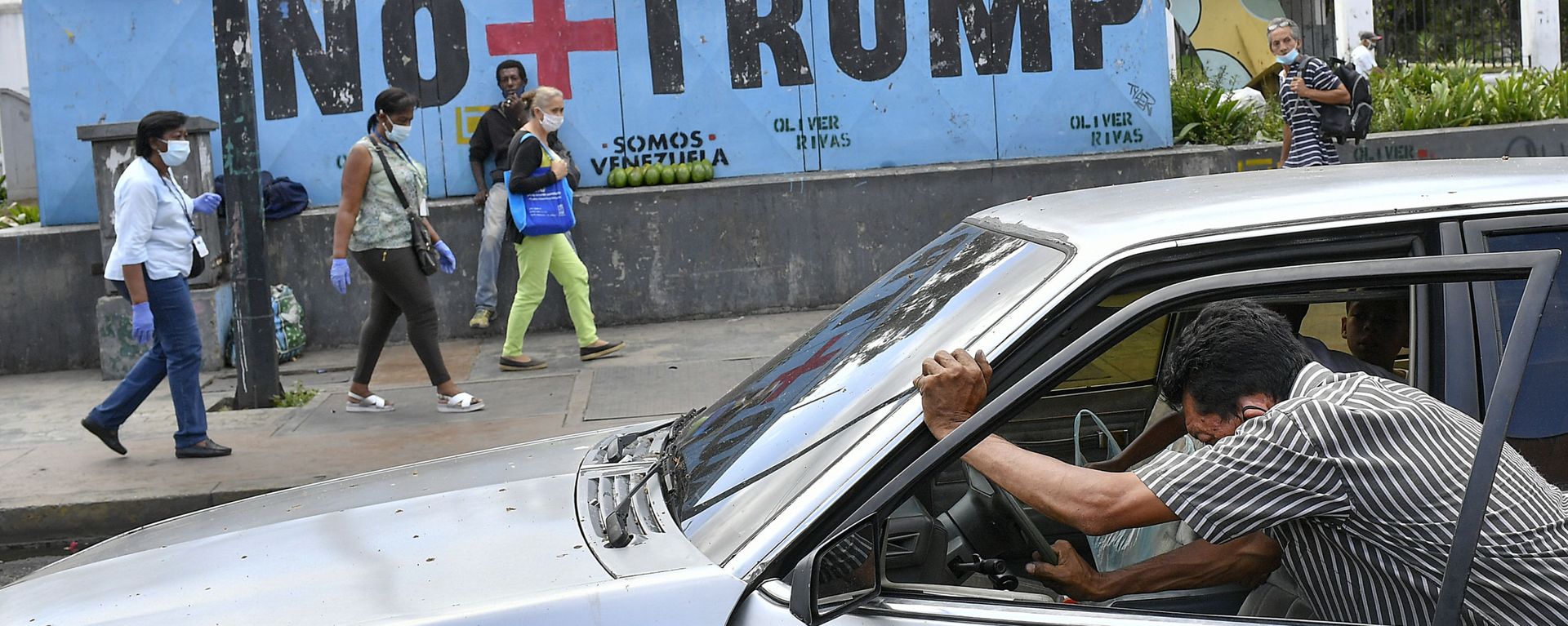 A man pushes his car that ran out of gas as people wearing protective face masks as a precaution against the spread of the new coronavirus, walk past a mural with a message that reads in Spanish: No more Trump in Caracas, Venezuela, Sunday, Nov. 8, 2020. Venezuelan President Nicolas Maduro has sent a congratulatory message to U.S. President-elect Joe Biden who won the U.S. presidential election, defeating incumbent Donald Trump. A man pushes his car that ran out of gas as people wearing protective face masks as a precaution against the spread of the new coronavirus, walk past a mural with a message that reads in Spanish: No more Trump in Caracas, Venezuela, Sunday, Nov. 8, 2020. Venezuelan President Nicolas Maduro has sent a congratulatory message to U.S. President-elect Joe Biden who won the U.S. presidential election, defeating incumbent Donald Trump. - Sputnik International, 1920, 19.01.2025