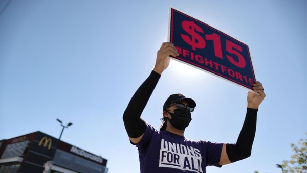A man holds up a minimum wage sign at a rally held by fast food workers and supporters to celebrate the California Labor Commissioner’s order for the company to rehire and compensate workers who went on strike for coronavirus disease (COVID-19) protections, in Los Angeles, California, U.S., February 18, 2021. REUTERS/Lucy Nicholson - Sputnik International