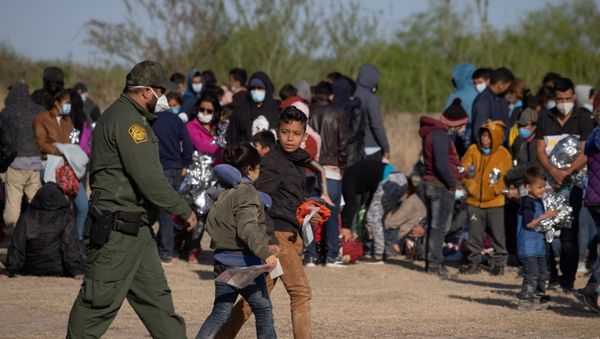 A U.S. Border Patrol Agent escorts two asylum-seeking unaccompanied minors from Central America as others take refuge near a baseball field after crossing the Rio Grande river into the United States from Mexico on rafts, in La Joya, Texas, U.S., March 19, 2021 - Sputnik International