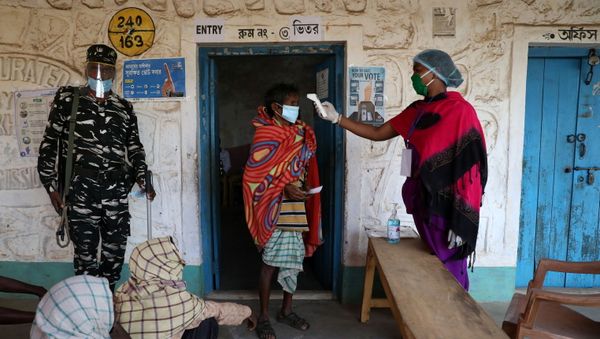 A woman checks the temperature of a voter before he casts his vote at a polling booth during the first phase of the West Bengal state election in Purulia district, India, 27 March 2021. - Sputnik International