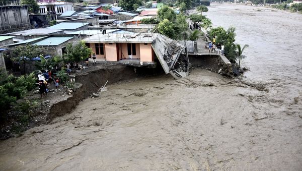 Residents stand along the water's edge by damaged homes after heavy rains and strong winds lashed East Timor's capital Dili overnight causing extensive flooding on April 4, 2021 - Sputnik International