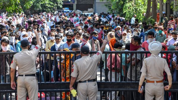 Police personnel stand guard as stranded migrant workers and their families wait to get thermally screened behind the gate of the Guru Nanak Auditorium before going to a railway station to take a train to Bhagalpur in Bihar state back to their hometowns after the government eased a nationwide lockdown imposed as a preventive measure against the COVID-19 coronavirus, in Amritsar on May 17, 2020.  - Sputnik International