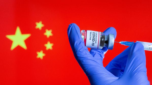 FILE PHOTO: FILE PHOTO: A woman holds a small bottle labeled with a Coronavirus COVID-19 Vaccine sticker and a medical syringe in front of displayed China flag in this illustration taken, October 30, 2020 - Sputnik International