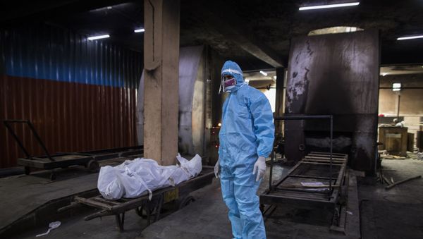 A relative wearing Personal Protective Equipment (PPE) stands next to the body of a person who died from the COVID-19 coronavirus before cremation in a furnace at the Nigambodh Ghat cremation ground, in New Delhi on 22 August 2020. - Sputnik International