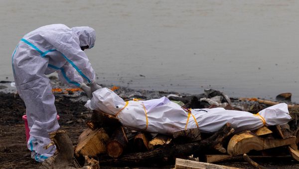 A man wearing a protective suit touches the body of his relative, who died from the coronavirus disease (COVID-19), before his cremation on the banks of the river Ganges at Garhmukteshwar in the northern state of Uttar Pradesh, India, May 6, 2021. - Sputnik International