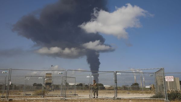 An Israeli soldier stands guard next to an Iron Dome air defense system as smoke rises from an oil tank on fire after it was hit by a rocket fire from Gaza Strip, near the town of Ashkelon, Israel,, Wednesday, May 12, 2021 - Sputnik International