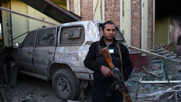 An Afghan security official stands alert among damaged buildings and a vehicle after a car bomb attack near the Spanish embassy compound in Kabul on December 12, 2015 - Sputnik International