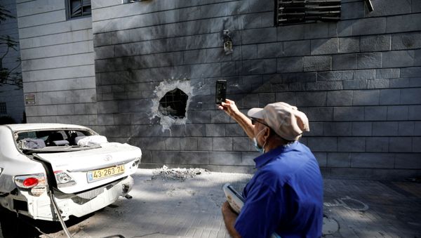 An Israeli man takes a photo with his mobile phone at a residential building after a rocket launched overnight from the Gaza Strip hit it in Ashkelon, Israel May 14, 2021. - Sputnik International