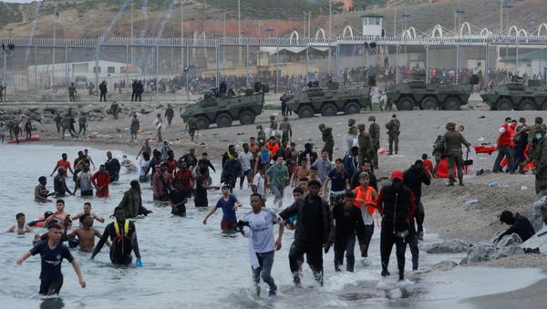 Moroccan citizens walk in the water as Spanish legionnaires patrol the area near the fence on a beach in El Tarajal, after thousands swam across the Spanish-Moroccan border on Monday, in Ceuta, Spain, May 18, 2021. REUTERS/Jon Nazca - Sputnik International