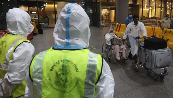 Indian municipal workers in personal protective equipment (PPE) watch as a passenger on wheelchair arrives from United Kingdom, at Chhatrapati Shivaji Maharaj International Airport in Mumbai, India, Tuesday, Dec. 22, 2020 - Sputnik International