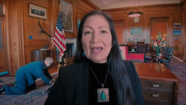 Late Night With Seth Meyers video clip screenshot showing a staffer crawling on the floor behind US Secretary of Interior Deb Haaland during the interview - Sputnik International