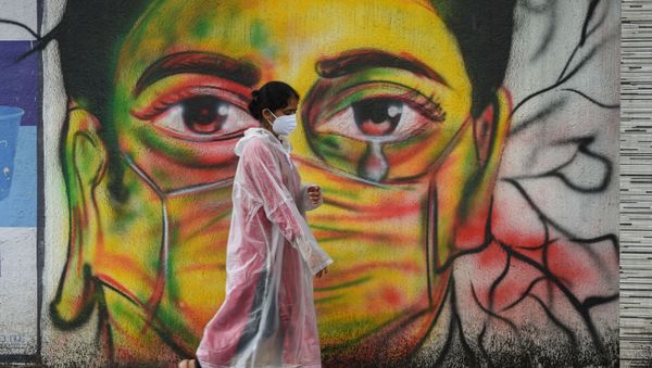 A woman wearing a raincoat walks past a mural depicting a woman with a facemask to spread awareness about the Covid-19 coronavirus, in Mumbai on June 17, 2021 - Sputnik International