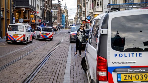 A woman walks past police vehicles parked on the site of an attack during which a Dutch journalist specialised in crime, Peter R. de Vries was seriously injured in a shooting in Amsterdam, on July 6, 2021. - Sputnik International
