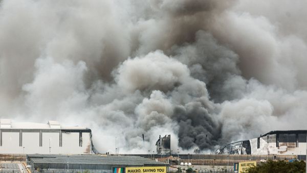 Smoke rises from a Makro building set on fire overnight in Umhlanga, north of Durban, on July 13, 2021 as several shops, businesses and infrastructure are damaged in the city, following four nights of continued violence and looting sparked by the jailing of ex-president Jacob Zuma. - The unrest erupted last on July 9 after Zuma started serving a 15-month term for snubbing a probe into the corruption that stained his nine years in power. In a nationwide address , current President Ramaphosa lashed opportunistic acts of criminality, with groups of people instigating chaos merely as a cover for looting and theft. - Sputnik International