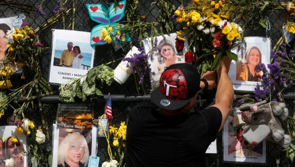 A man places flowers on a makeshift memorial for the victims of the Surfside's Champlain Towers South condominium collapse in Miami, Florida, U.S., July 8, 2021 - Sputnik International