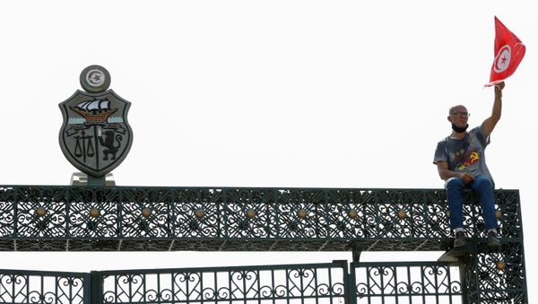 A supporter of Tunisia's biggest political party, the moderate Islamist Ennahda, holds a Tunisian flag as he sits atop the gate of the parliament building in Tunis, Tunisia July 26, 2021 - Sputnik International