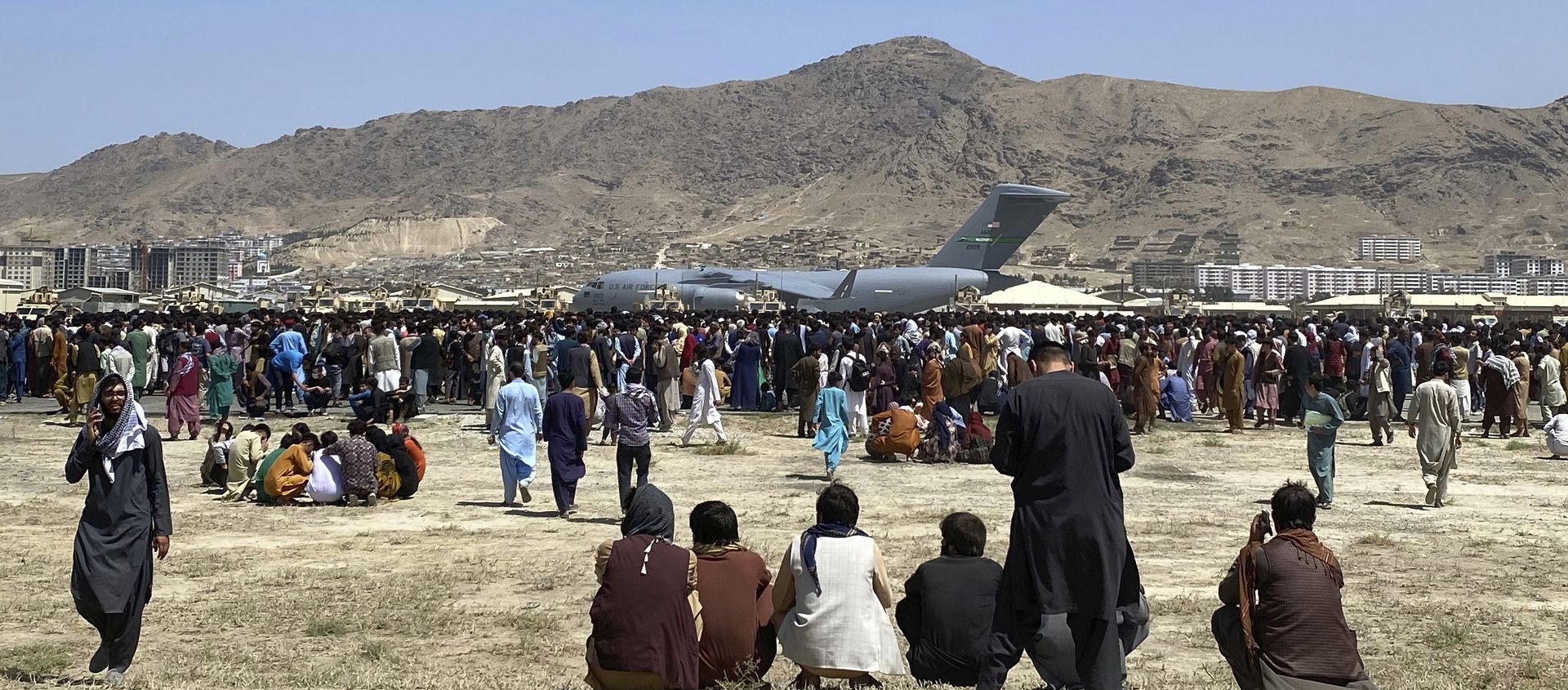 Hundreds of people gather near a U.S. Air Force C-17 transport plane at a perimeter at the international airport in Kabul, Afghanistan, Monday, Aug. 16, 2021. On Monday, the U.S. military and officials focus was on Kabul’s airport, where thousands of Afghans trapped by the sudden Taliban takeover rushed the tarmac and clung to U.S. military planes deployed to fly out staffers of the U.S. Embassy, which shut down Sunday, and others Hundreds of people gather near a U.S. Air Force C-17 transport plane at a perimeter at the international airport in Kabul, Afghanistan, Monday, Aug. 16, 2021. On Monday, the U.S. military and officials focus was on Kabul’s airport, where thousands of Afghans trapped by the sudden Taliban takeover rushed the tarmac and clung to U.S. military planes deployed to fly out staffers of the U.S. Embassy, which shut down Sunday, and others - Sputnik International, 1920