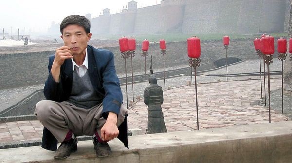A man sits near a gate to the ancient city of Pingyao, in northern China, 21 September, 2002, which is now one of China's top tourist destinations - Sputnik International