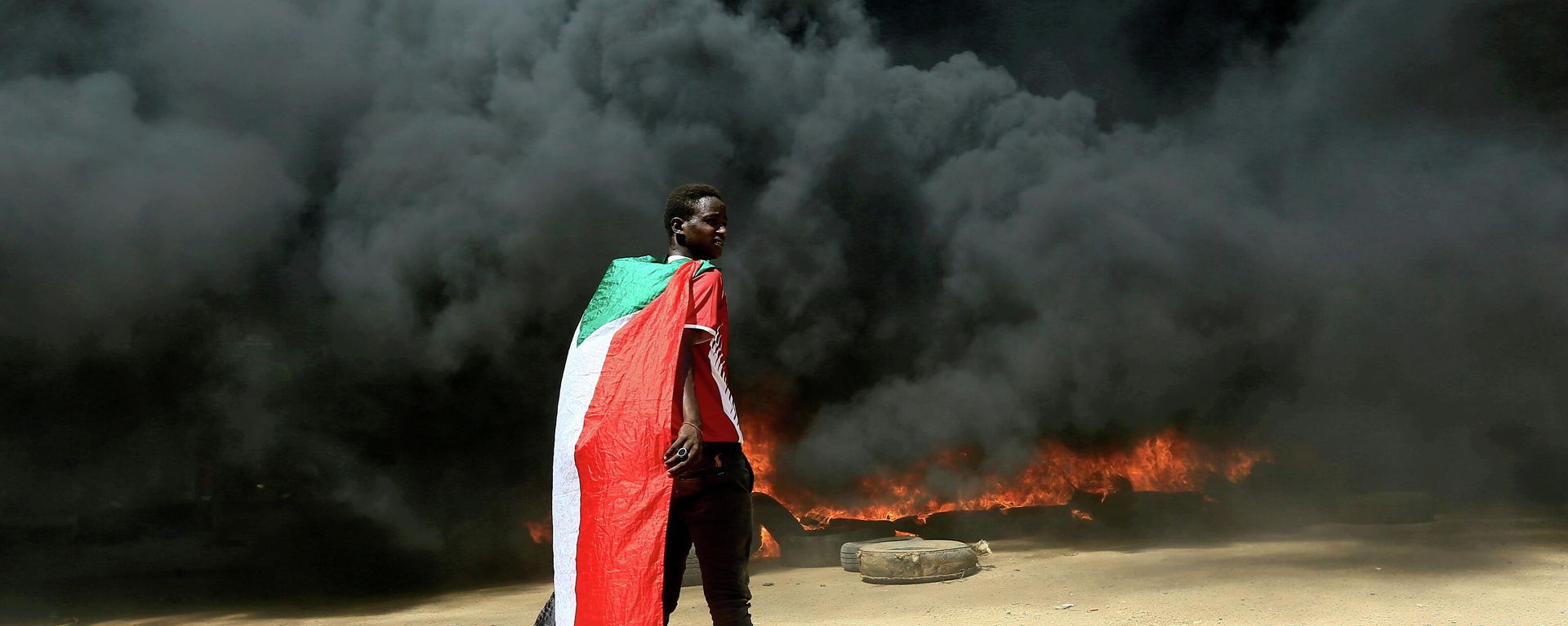 A person wearing a Sudan's flag stand in front of a burning pile of tyres during a protest against prospect of military rule in Khartoum, Sudan October 21, 2021. A person wearing a Sudan's flag stand in front of a burning pile of tyres during a protest against prospect of military rule in Khartoum, Sudan October 21, 2021. - Sputnik International, 1920, 24.11.2021