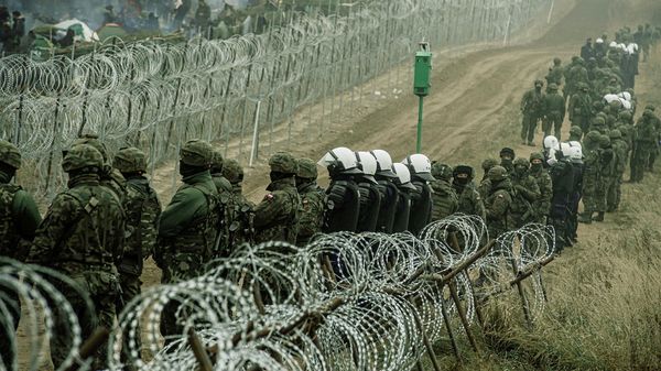 FILE PHOTO: Polish soldiers and police watch migrants at the Poland/Belarus border near Kuznica, Poland, in this photograph released by the Territorial Defence Forces, November 12, 2021. Picture taken November 11, 2021.  Irek Dorozanski/DWOT/Handout via REUTERS THIS IMAGE HAS BEEN SUPPLIED BY A THIRD PARTY/File Photo - Sputnik International